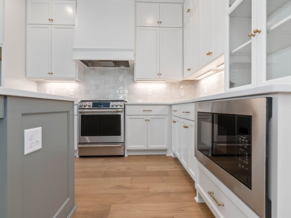 Modern white kitchen with wooden flooring and built-in appliances.