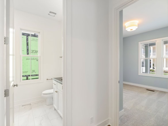 Bright bathroom with white fixtures and a view into a spacious bedroom.