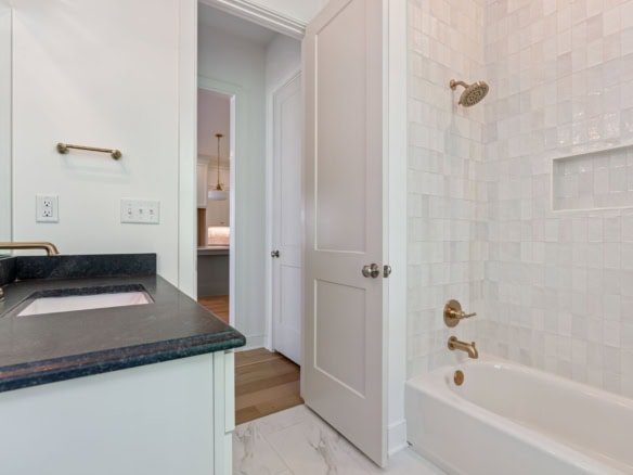 Bathroom with white tiles, bathtub, and gold fixtures.