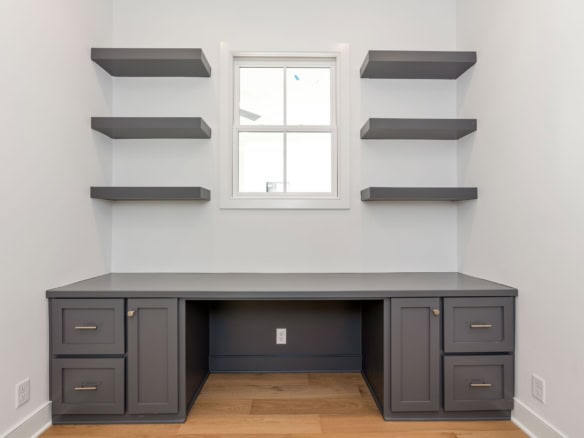 Custom built office desk with gray cabinetry and wall shelves.