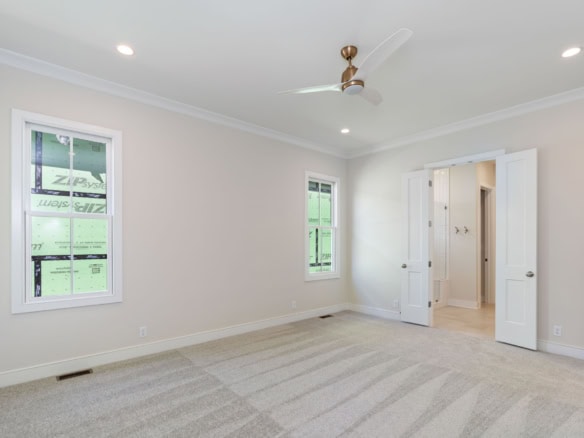Interior view of a newly built, spacious bedroom with white walls and carpet flooring.