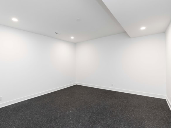 Interior room with white walls, ceiling, and dark carpet flooring.
