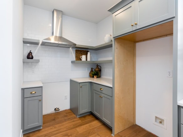 Newly renovated kitchen with gray cabinets, white backsplash, and wooden flooring.