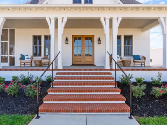 Front porch with brick stairs, white siding, and outdoor seating area.