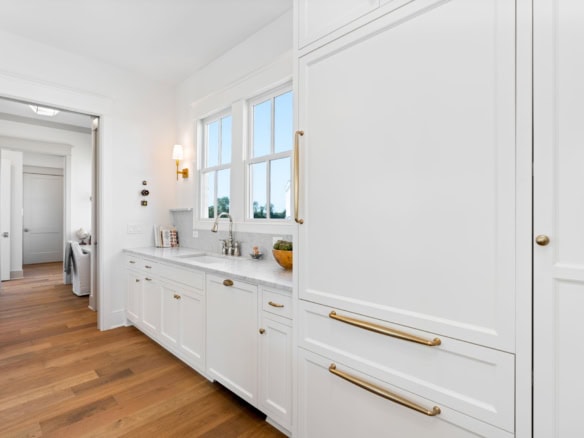 White kitchen cabinets with gold handles and a large window.