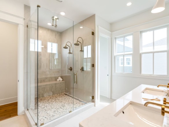 A sleek bathroom featuring a glass shower with multiple showerheads and a white vanity with gold fix.