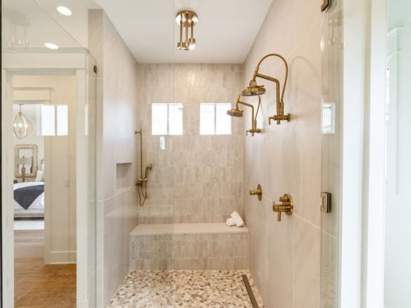 Elegant walk-in shower with multiple gold fixtures and natural light.