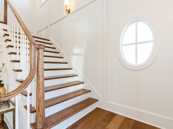 Interior staircase with wooden steps and white walls, natural light from round window.