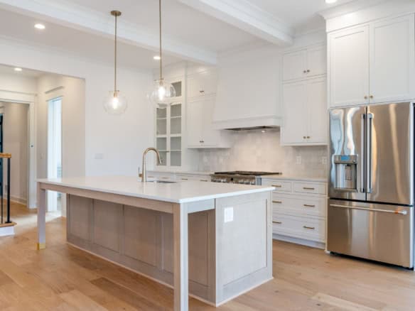Modern white kitchen with island, pendant lights, and stainless steel refrigerator.