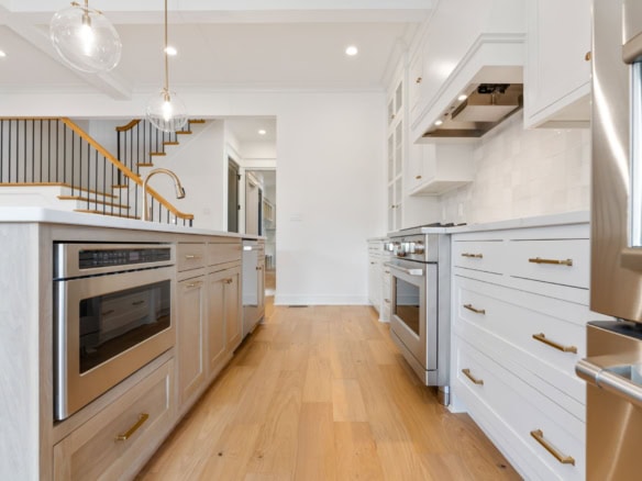 Bright modern kitchen with white cabinets, stainless steel appliances, and wooden flooring.