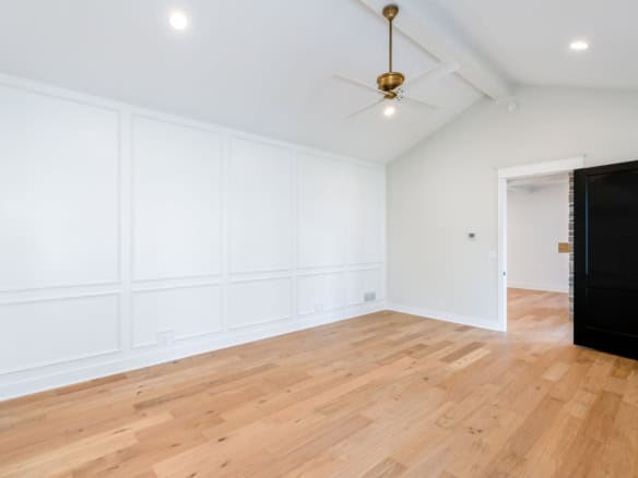 Interior of a new home with white paneled walls, hardwood flooring, and ceiling fan.