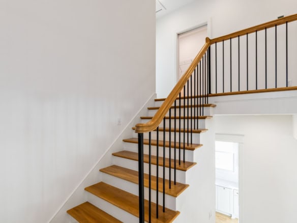 Interior staircase with wooden steps and black metal railing.