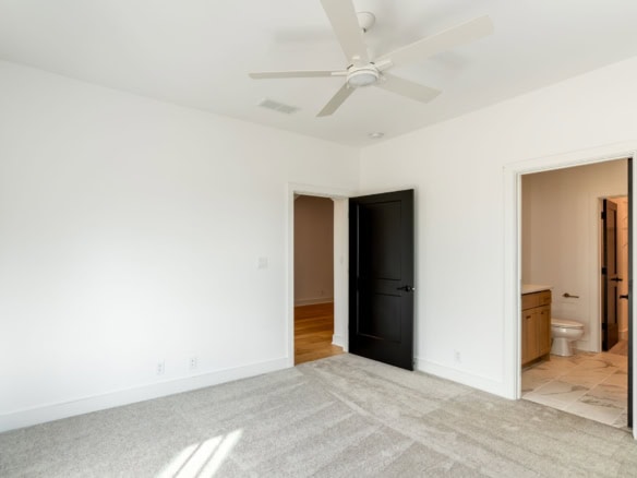 Bright, spacious bedroom with white walls, ceiling fan, and adjacent bathroom.