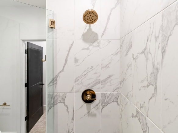 Elegant marble shower with gold showerhead and control handle.