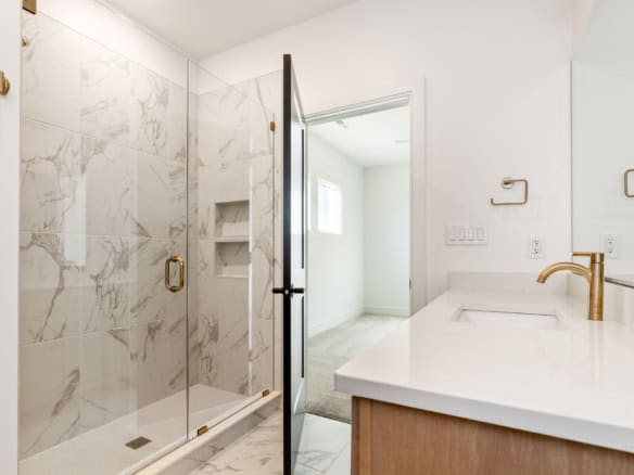 Bathroom with marble shower, white countertop, and gold fixtures.