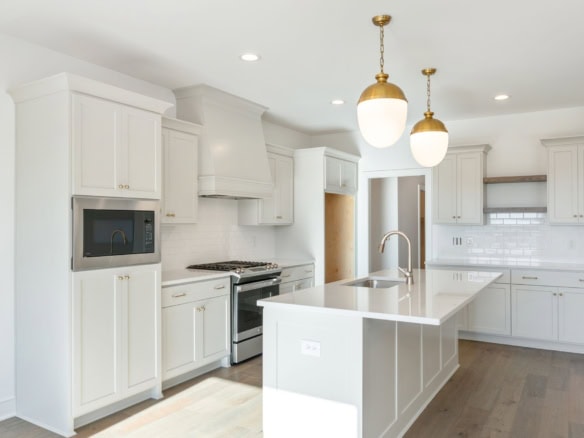 Bright white kitchen with island, pendant lights, and modern appliances in a new home.