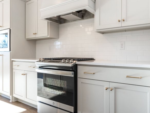 Modern white kitchen featuring a stainless steel stove and white cabinetry. Bright, clean design wit.