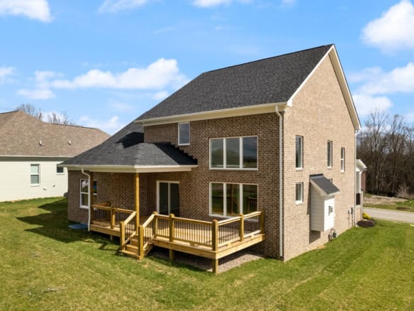 Brick house with a spacious wooden deck in a suburban neighborhood.