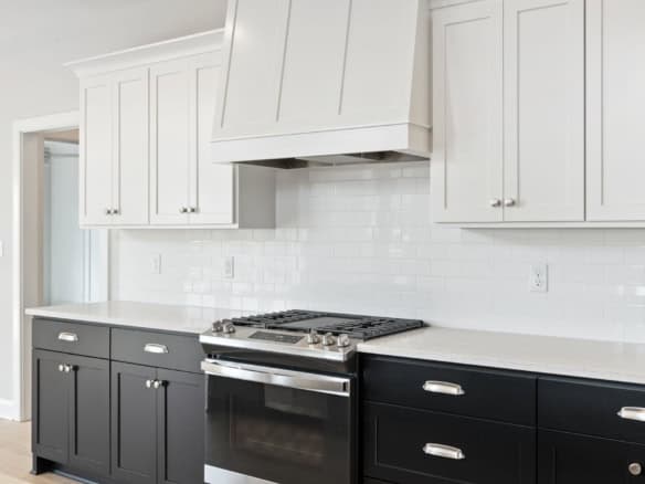 Beautiful kitchen with white upper cabinets, black lower cabinets, and a stainless steel stove.