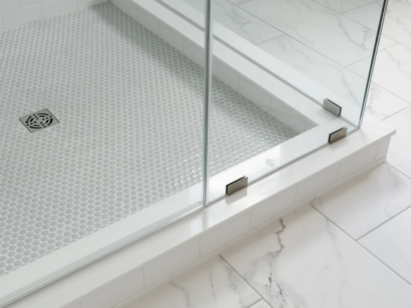 Glass shower with metal hinges and marble tile flooring.