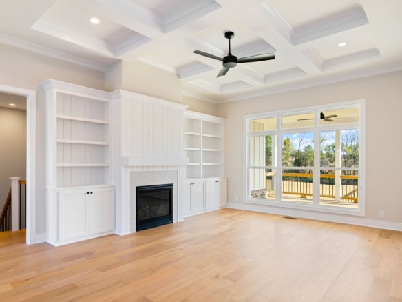 Spacious living room featuring a cozy fireplace, custom white built-in shelves, and large windows ov.