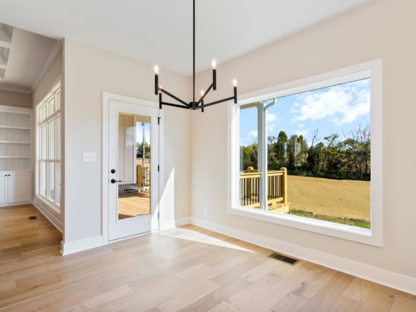 Bright living space with expansive windows overlooking a lush backyard. Elegant chandelier and hardw.