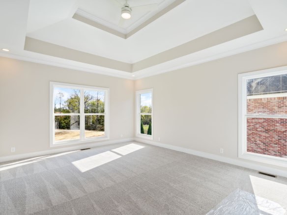 Interior view of a spacious, bright living room with large windows and a tray ceiling.