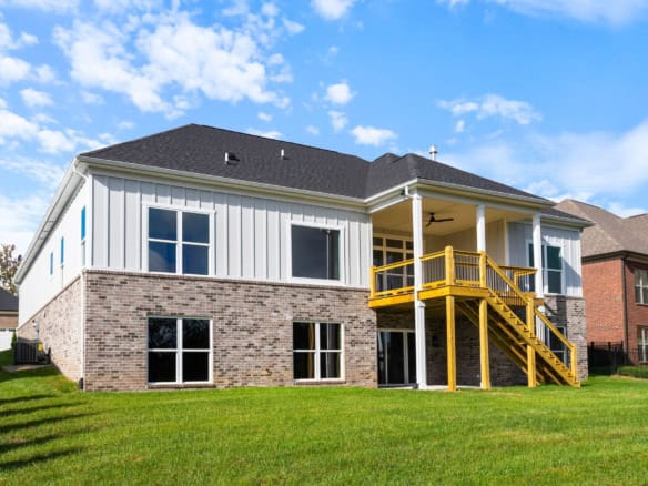 New construction home with brick and siding, featuring a wooden deck and large windows.