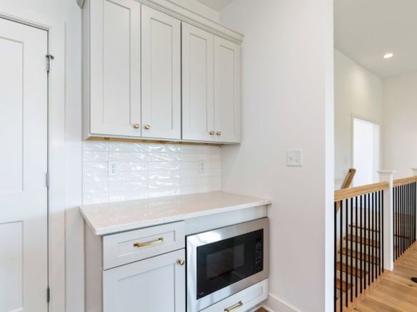 Bright white kitchen cabinets with gold hardware and a microwave.