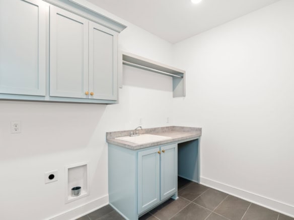 Bright laundry room featuring light blue cabinets and a marble countertop.