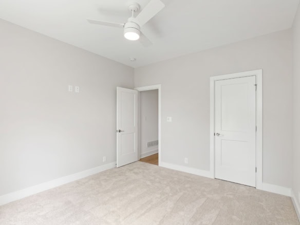 Interior bedroom with white walls, ceiling fan, and beige carpet flooring.