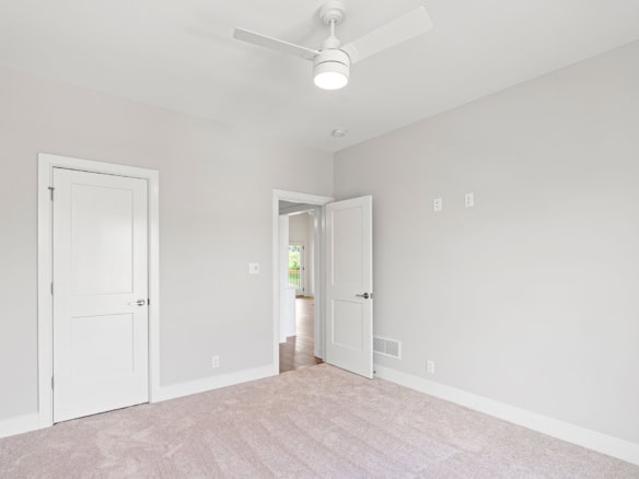 Interior bedroom with neutral walls, ceiling fan, and doorway to another room.