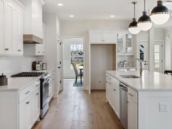 White kitchen with island and pendant lighting, featuring sleek cabinetry and stainless steel applia.