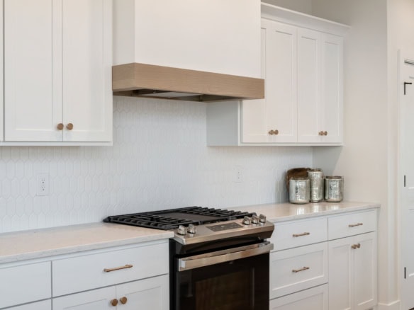 Bright white kitchen with gas stove, wooden range hood, and ample cabinetry.