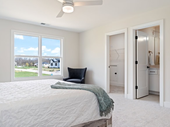 Bright bedroom featuring a large window overlooking a suburban neighborhood, with a walk-in closet a.