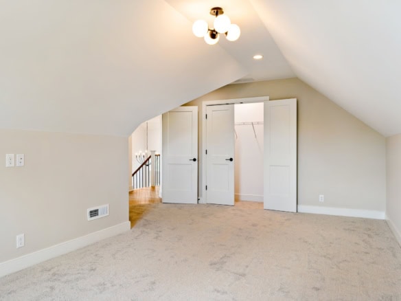 Attic bedroom featuring white closet doors and neutral wall colors, perfect for a cozy and functiona.