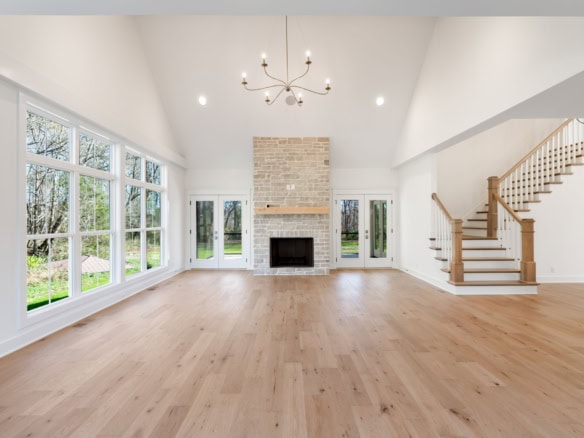 Spacious living room featuring a brick fireplace, abundant natural light from large windows, and har.