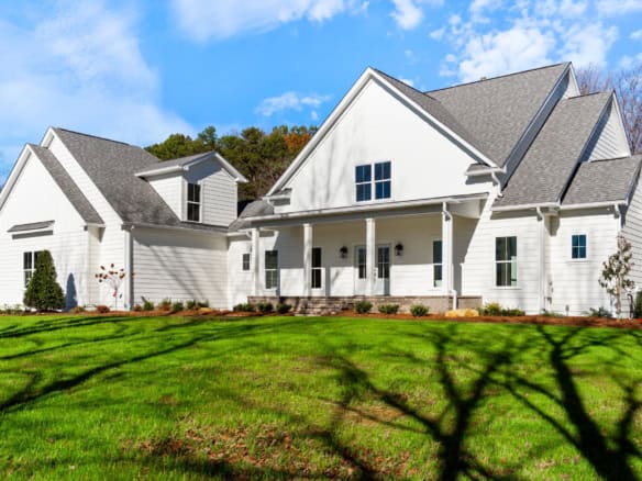 White house with a spacious front porch and multiple gabled roofs.