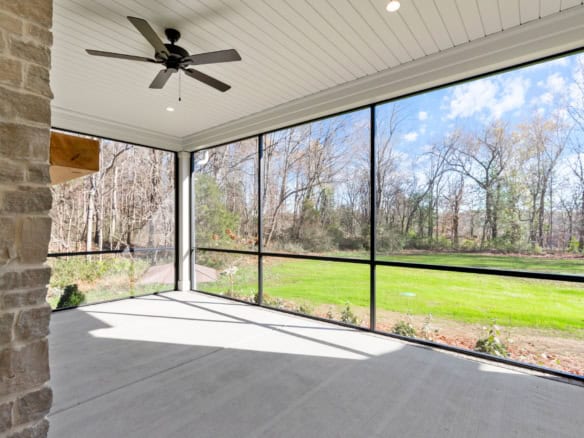 Spacious screened porch featuring a ceiling fan and large windows overlooking lush greenery and tree.