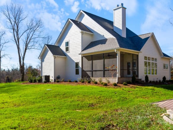 Beautiful white house with spacious yard and screened porch in a suburban setting.
