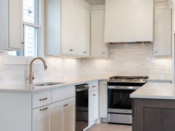 Bright, clean kitchen featuring white cabinets, a subway tile backsplash, and stainless steel stove.