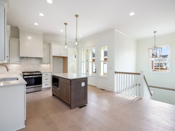 Modern white kitchen featuring a central island, stainless steel appliances, and abundant natural li.