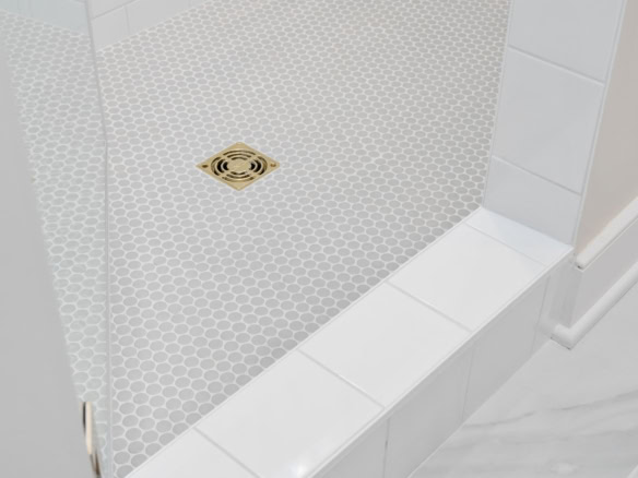 Bathroom shower floor with white hexagon tiles and a gold drain.