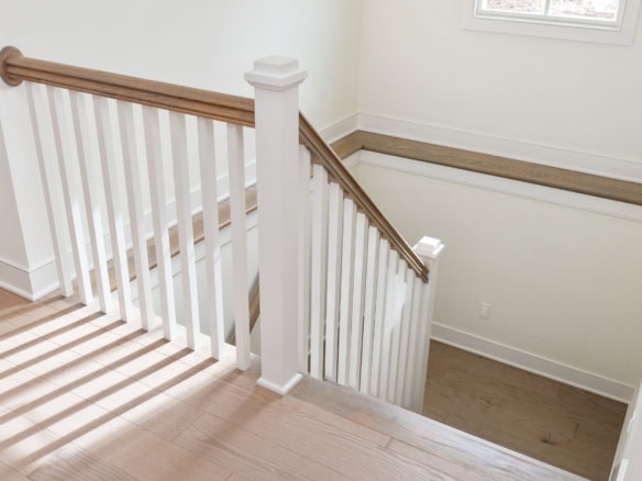 Interior view of a staircase with white balusters and wooden handrail.