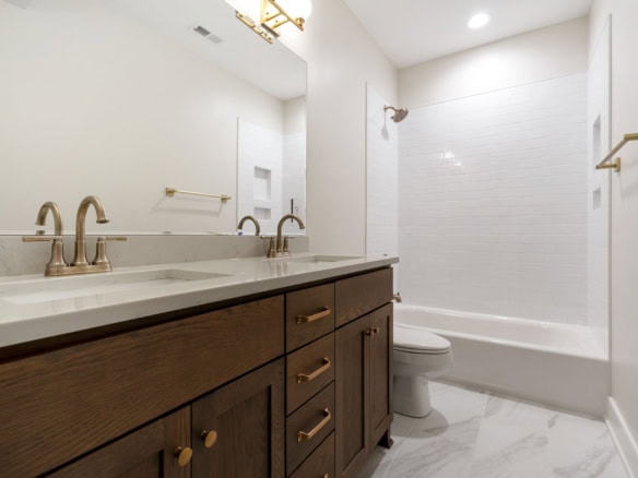 Dual-sink bathroom vanity with wooden cabinets and gold fixtures.