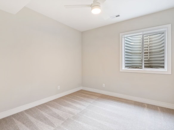 Bright empty bedroom with window and beige carpet flooring.