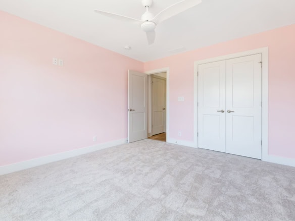 Pink bedroom with white closet doors and ceiling fan.