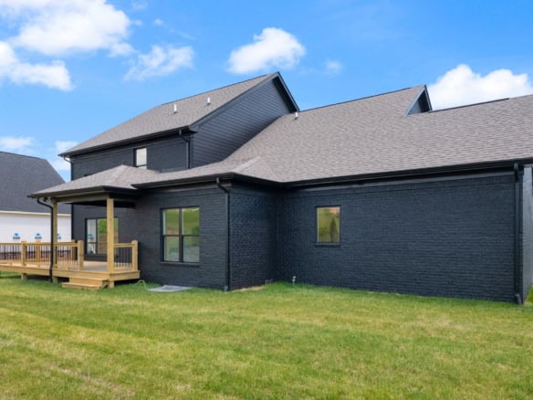 Black brick house with a wooden deck and lush green lawn.