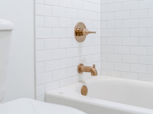Bathroom with white tiles and gold bathtub faucet and showerhead.