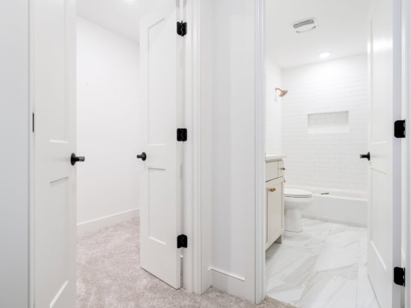 Interior view of a modern bathroom and closet with white walls and doors.